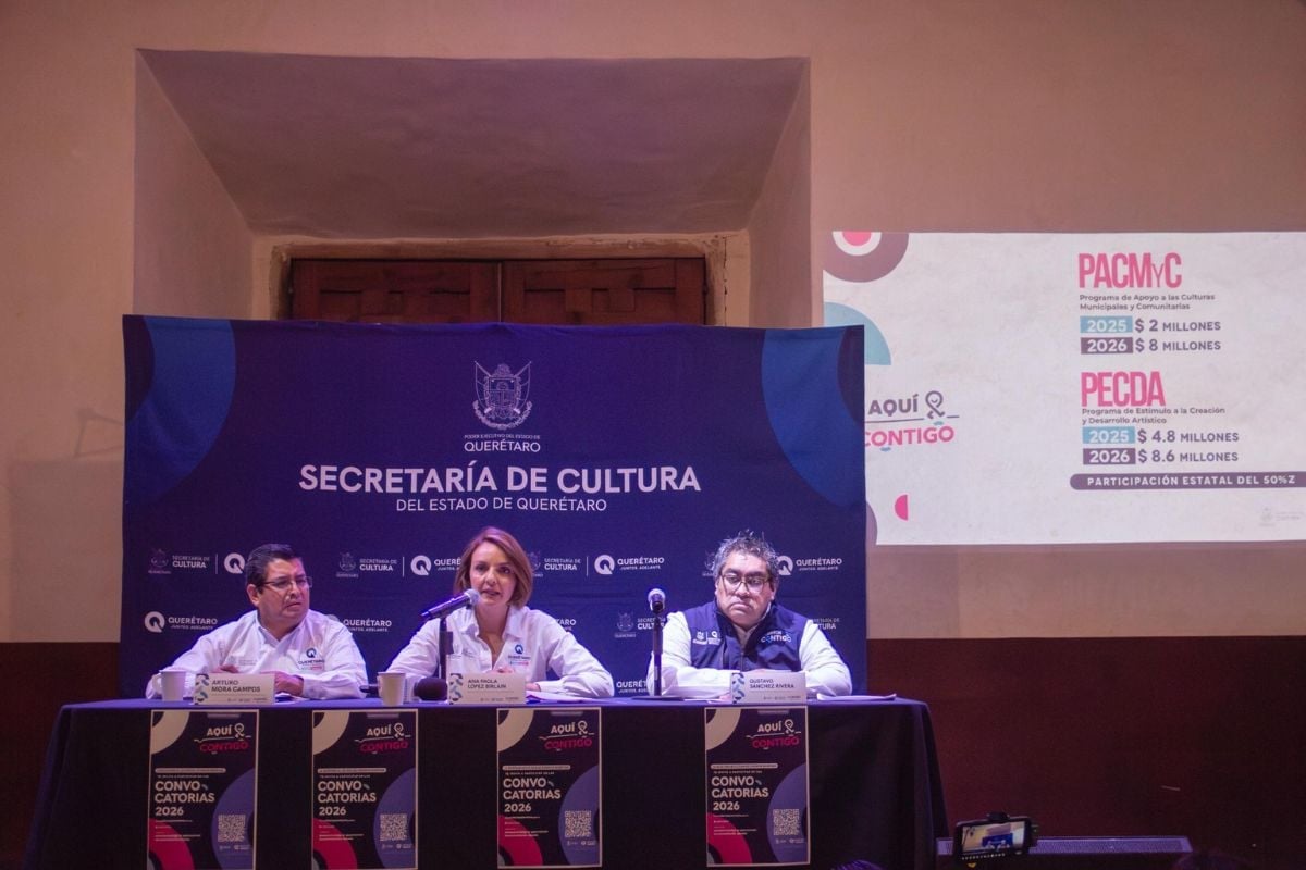 Three people sitting at a panel table under a purple Secretaría de Cultura banner during a presentation or conference