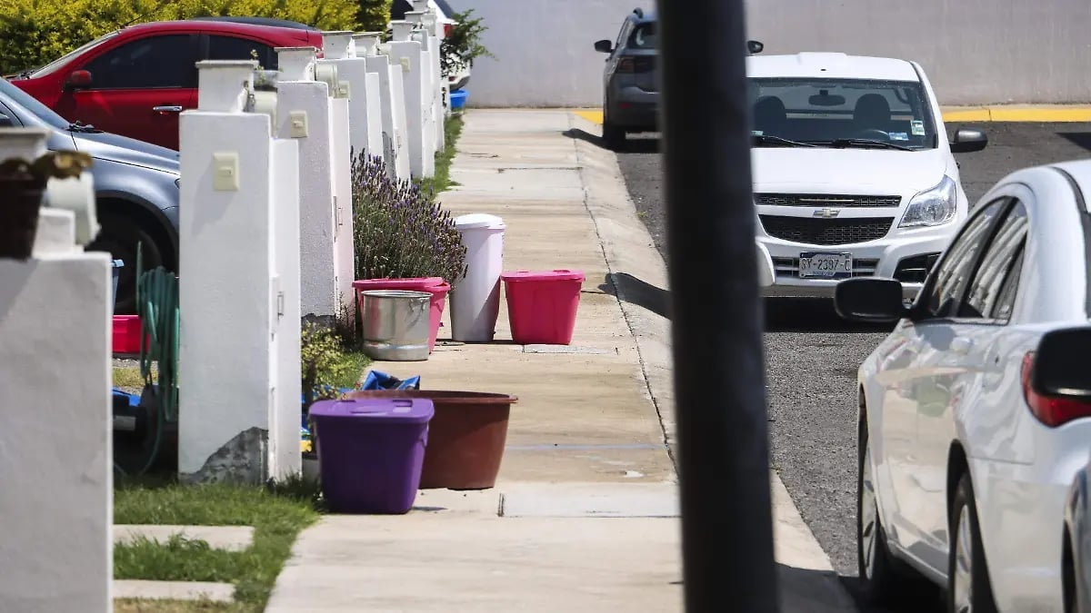 Residential driveway with parked vehicles, white fence, and colorful trash bins on concrete path